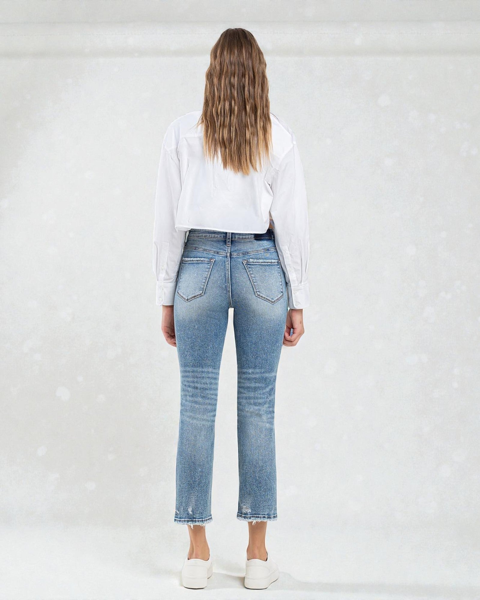 Person wearing blue jeans and a white shirt on a plain background