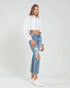 Woman wearing a white cropped top and ripped blue jeans on a white background