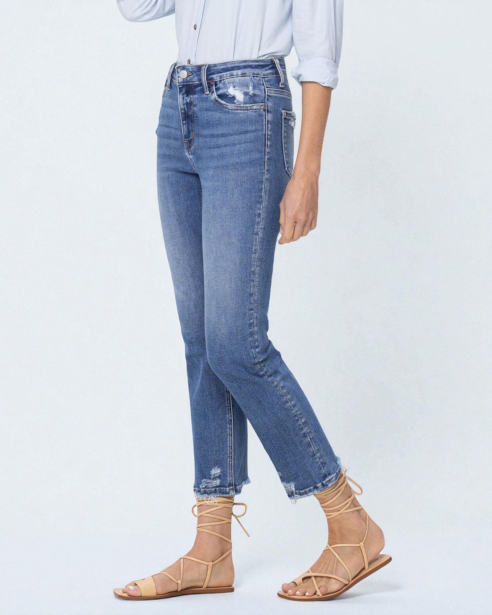 Person wearing blue jeans and beige sandals on a white background