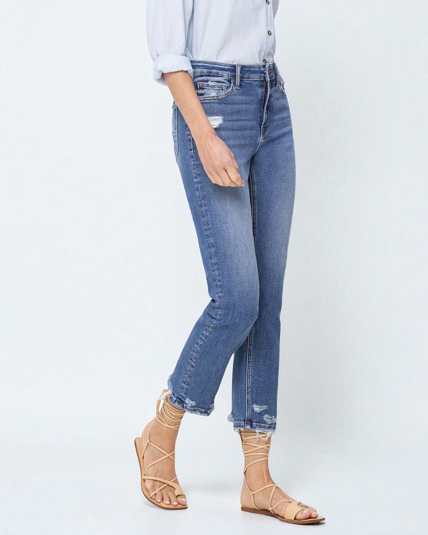 Person wearing blue jeans and beige sandals on a white background