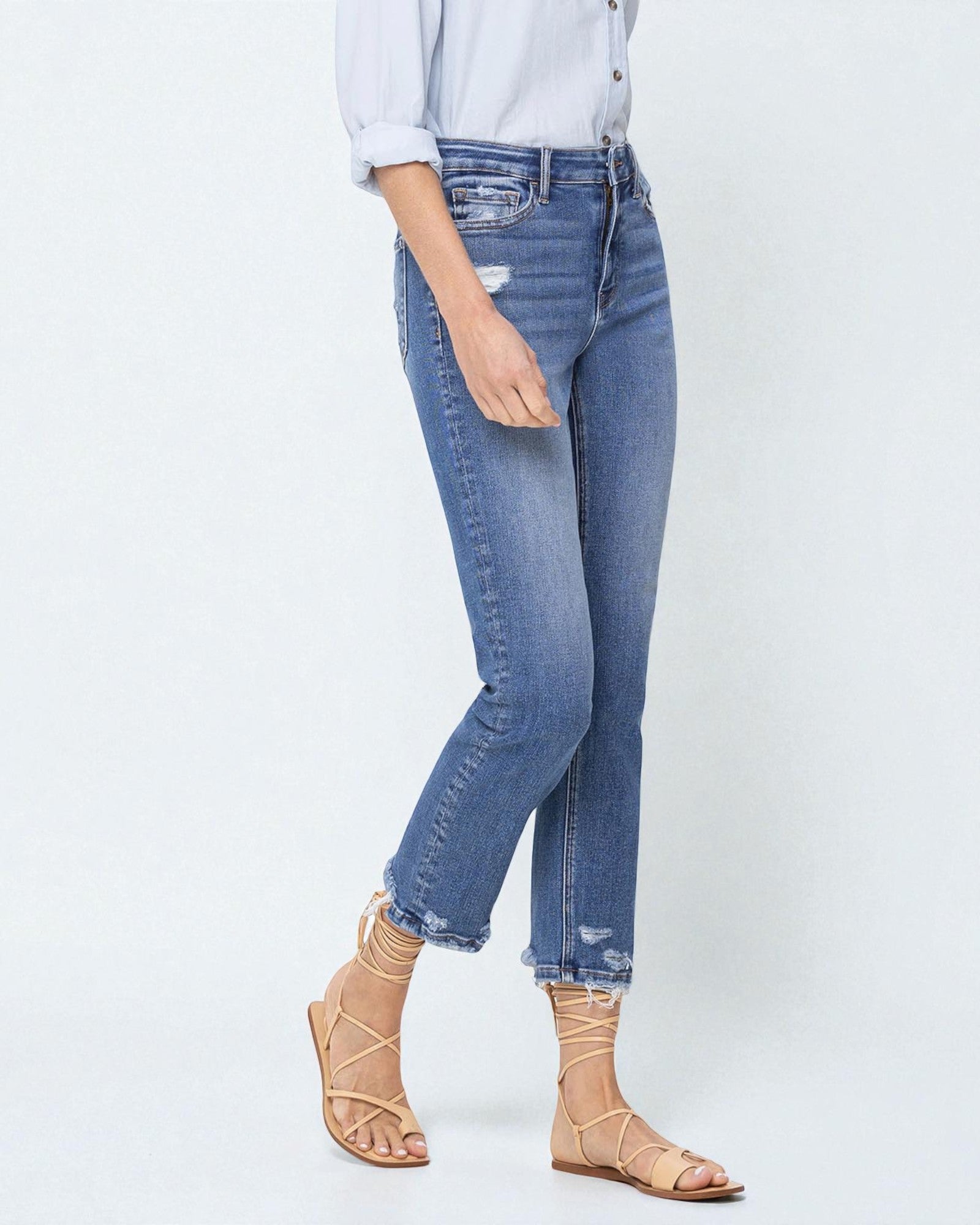 Person wearing blue jeans and beige sandals on a white background