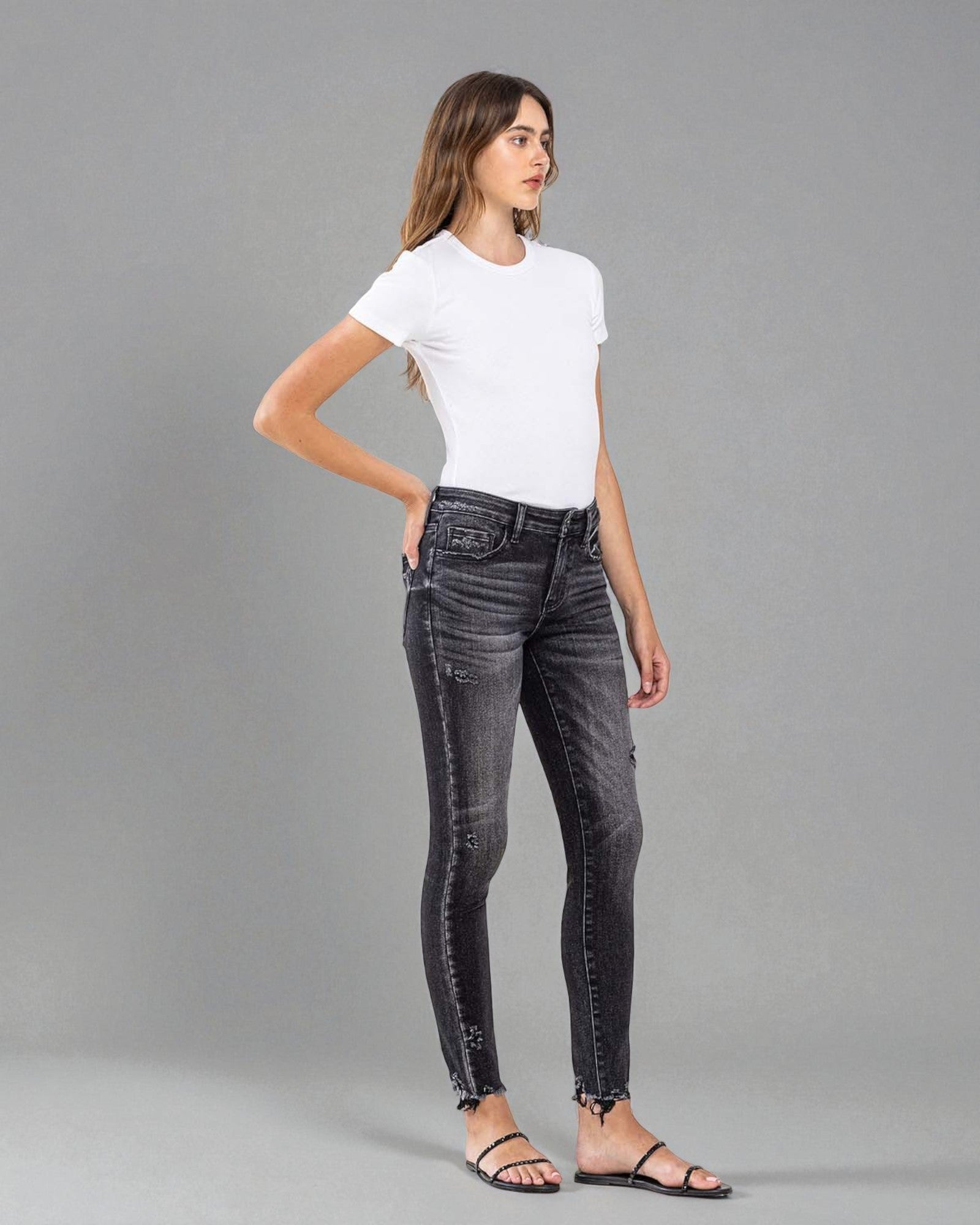 Woman wearing black jeans and a white t-shirt on a gray background