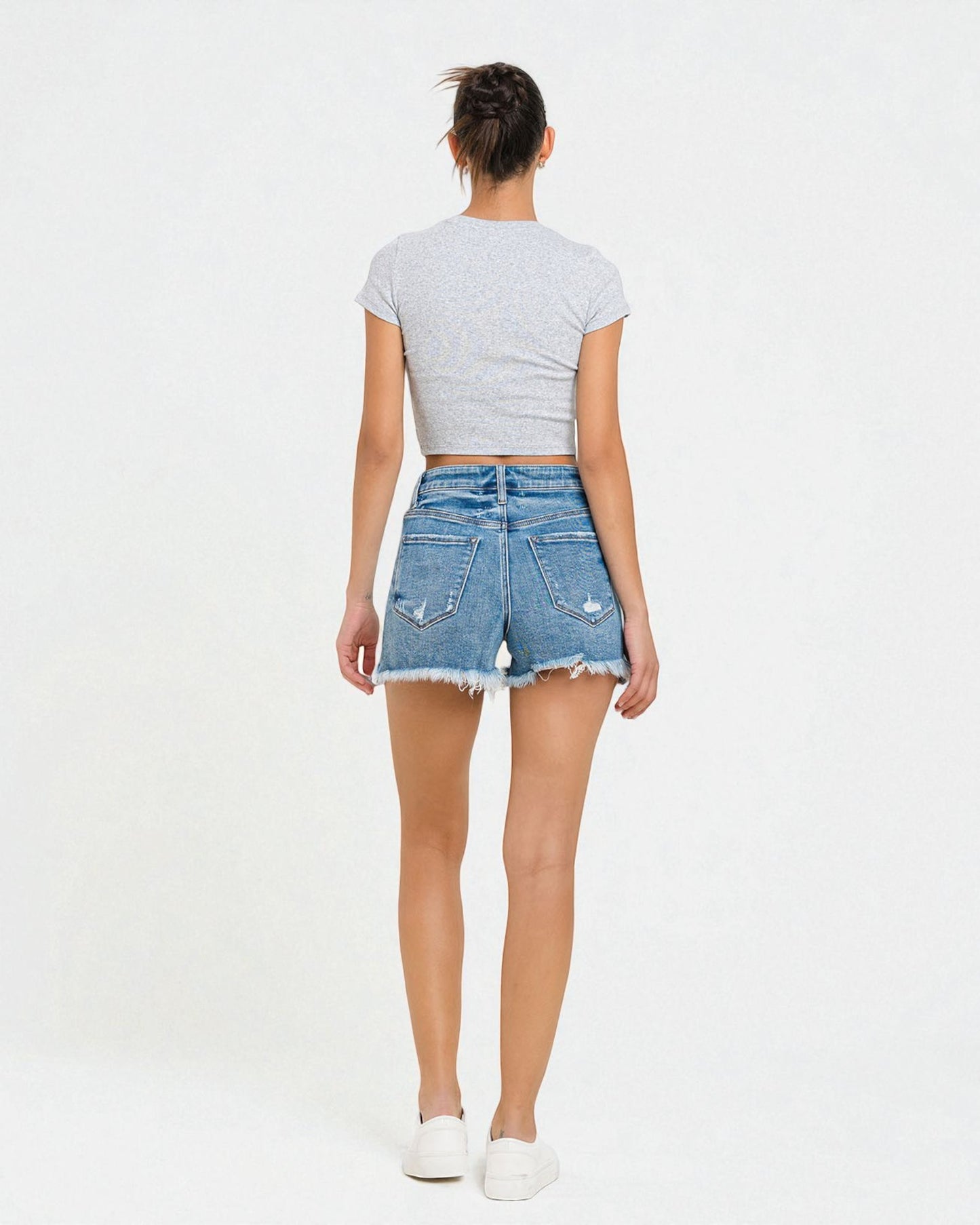 Person wearing a gray crop top and denim shorts on a white background