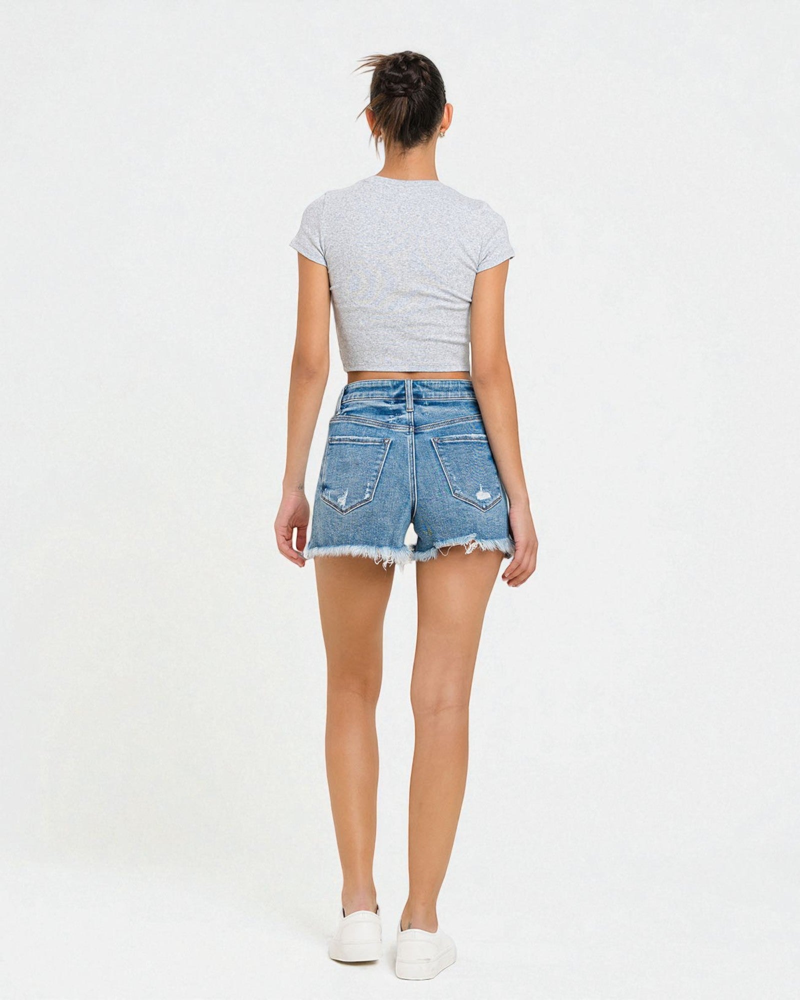Person wearing a gray crop top and denim shorts on a white background