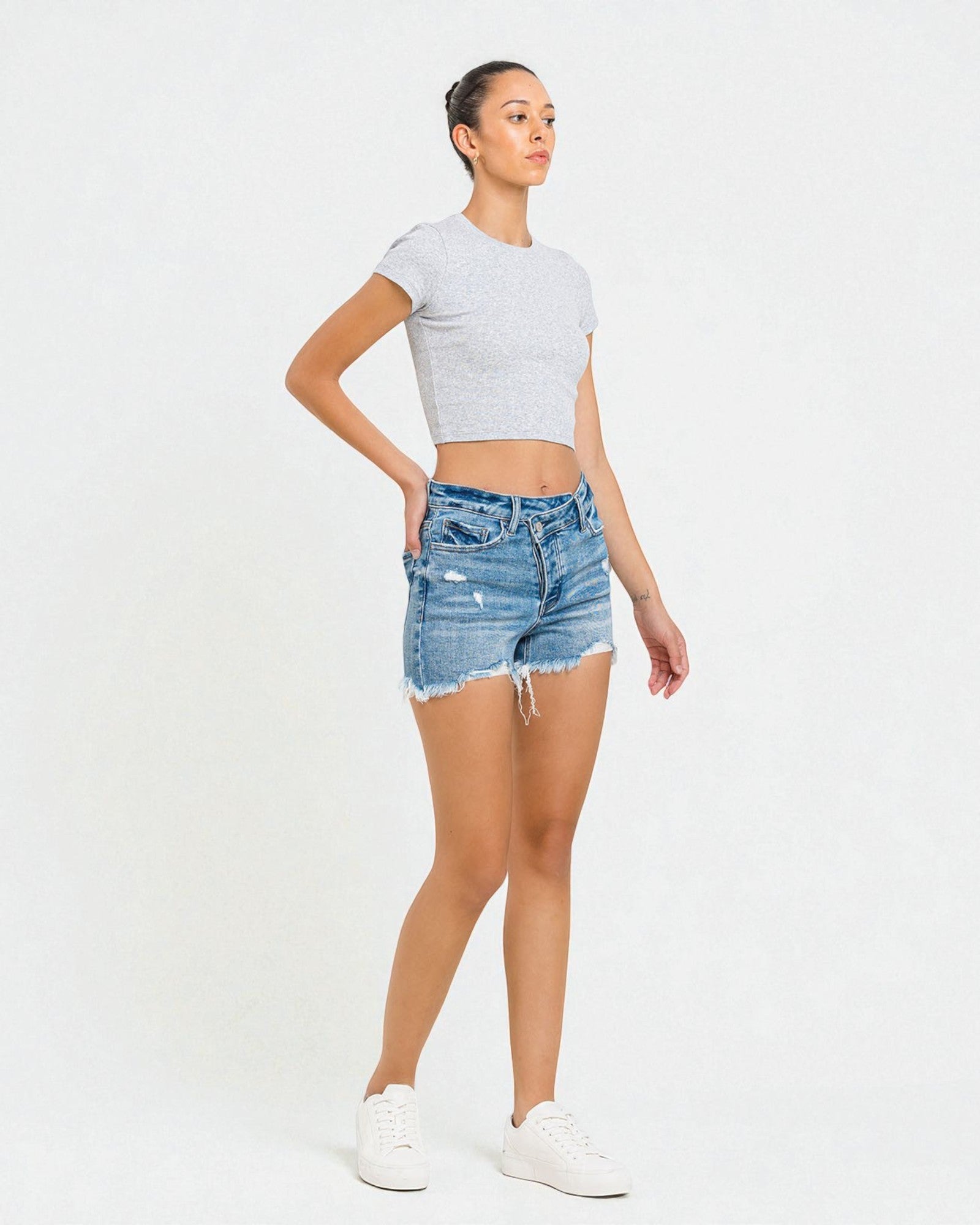 Woman wearing a gray crop top and denim shorts on a white background