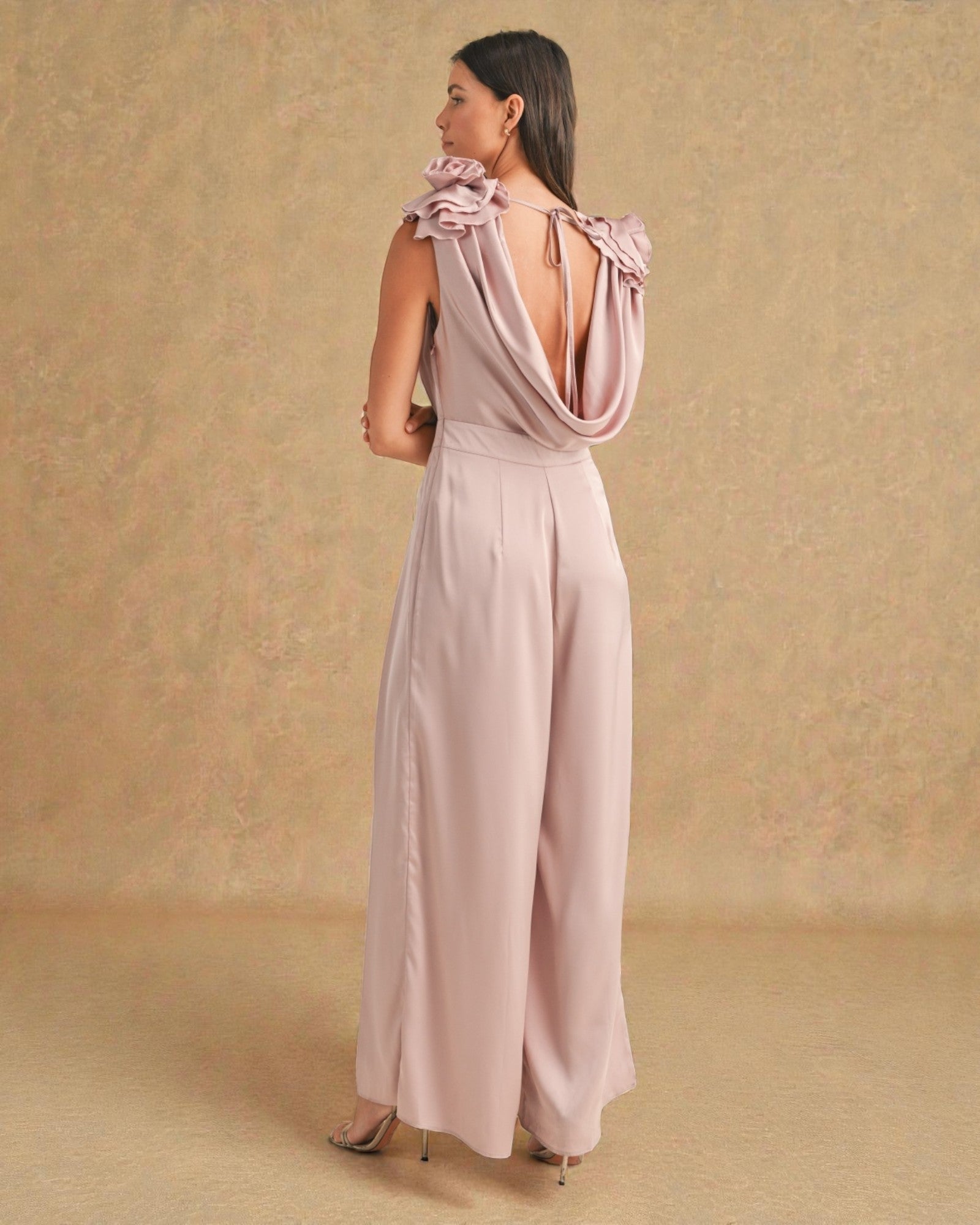 Woman wearing a light pink jumpsuit with bow details on a beige background