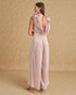 Woman wearing a light pink jumpsuit with bow details on a beige background