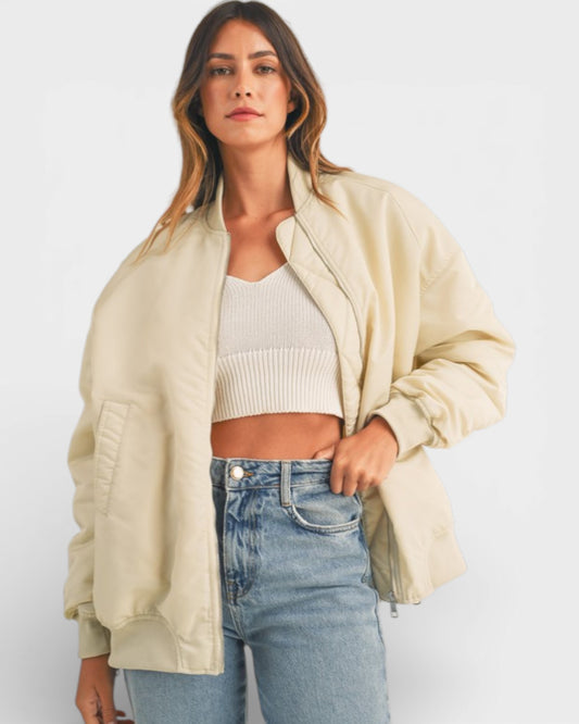 Woman wearing a beige jacket, white top, and blue jeans on a plain background