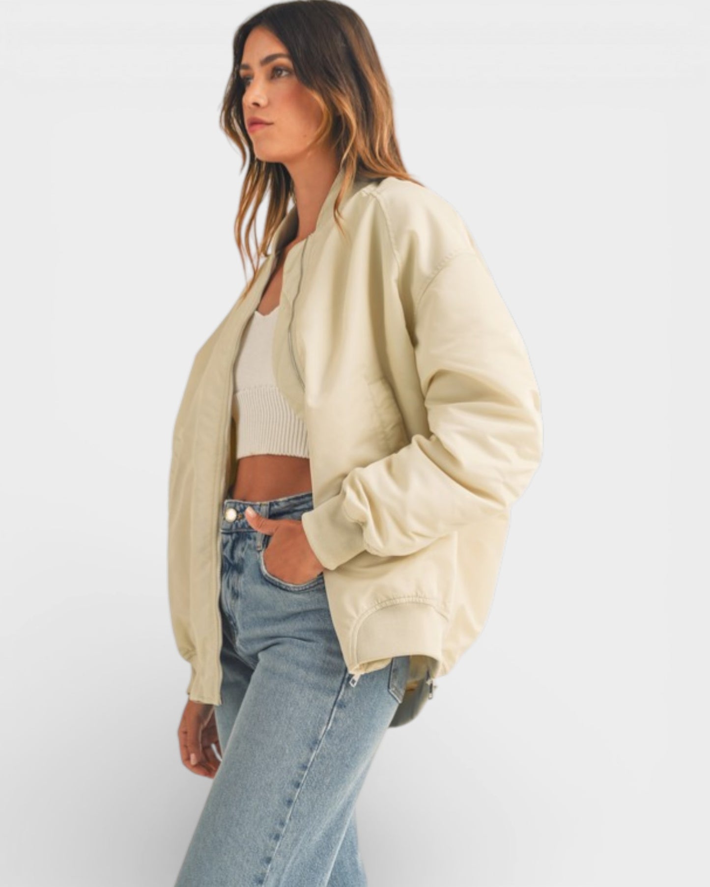 Woman wearing a beige cardigan, white top, and blue jeans on a white background