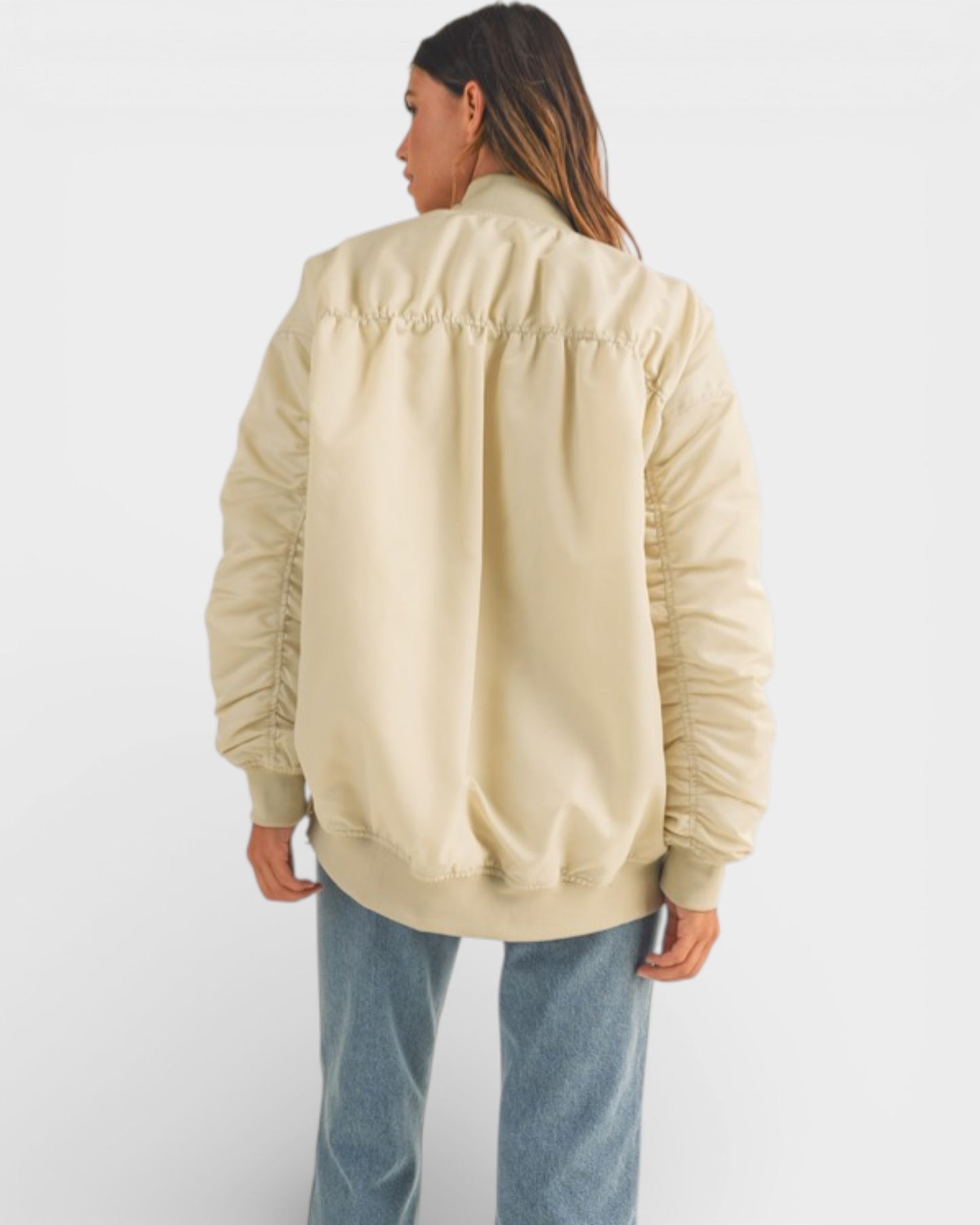 Person wearing a beige bomber jacket and blue jeans on a white background