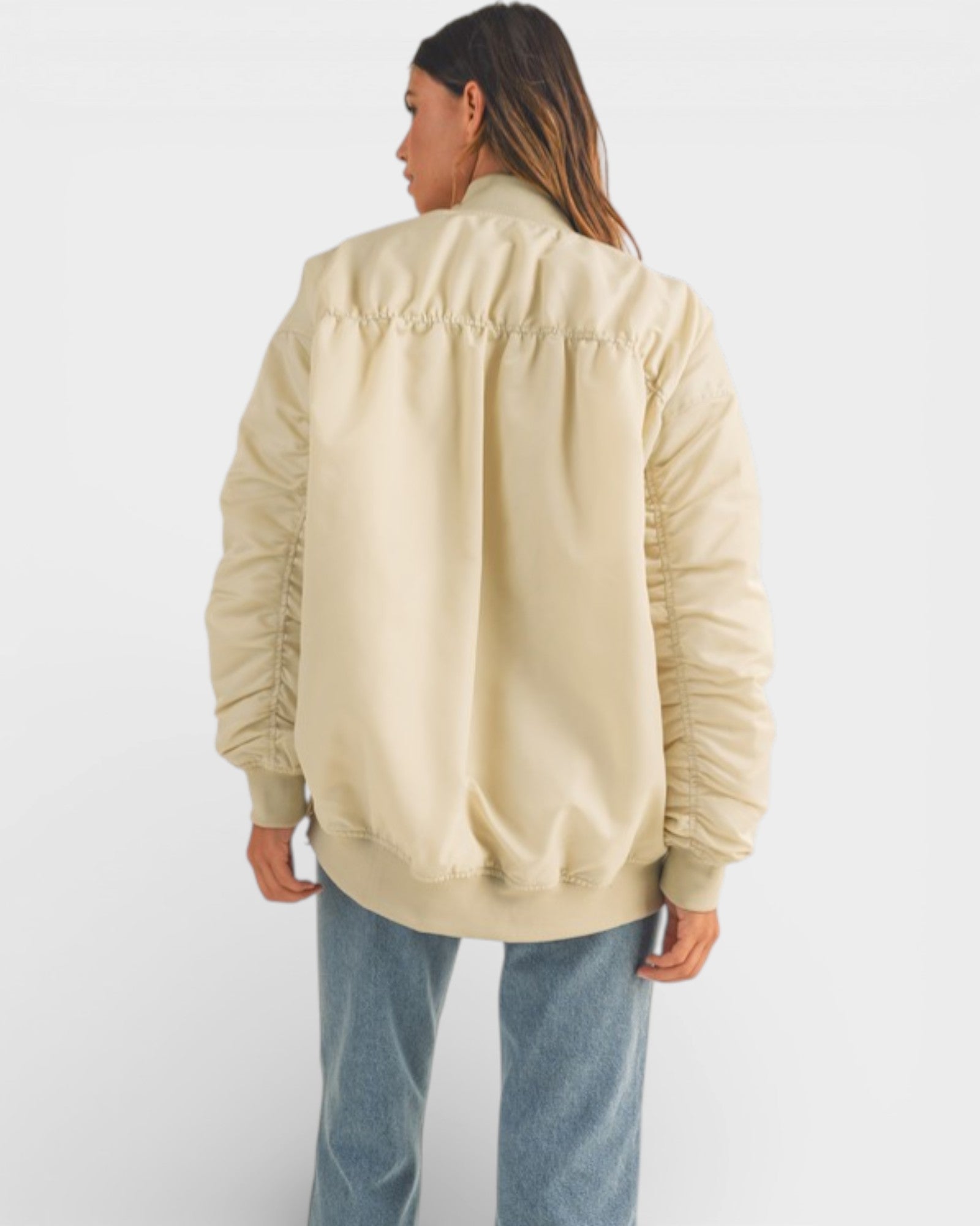Person wearing a beige bomber jacket and blue jeans on a white background