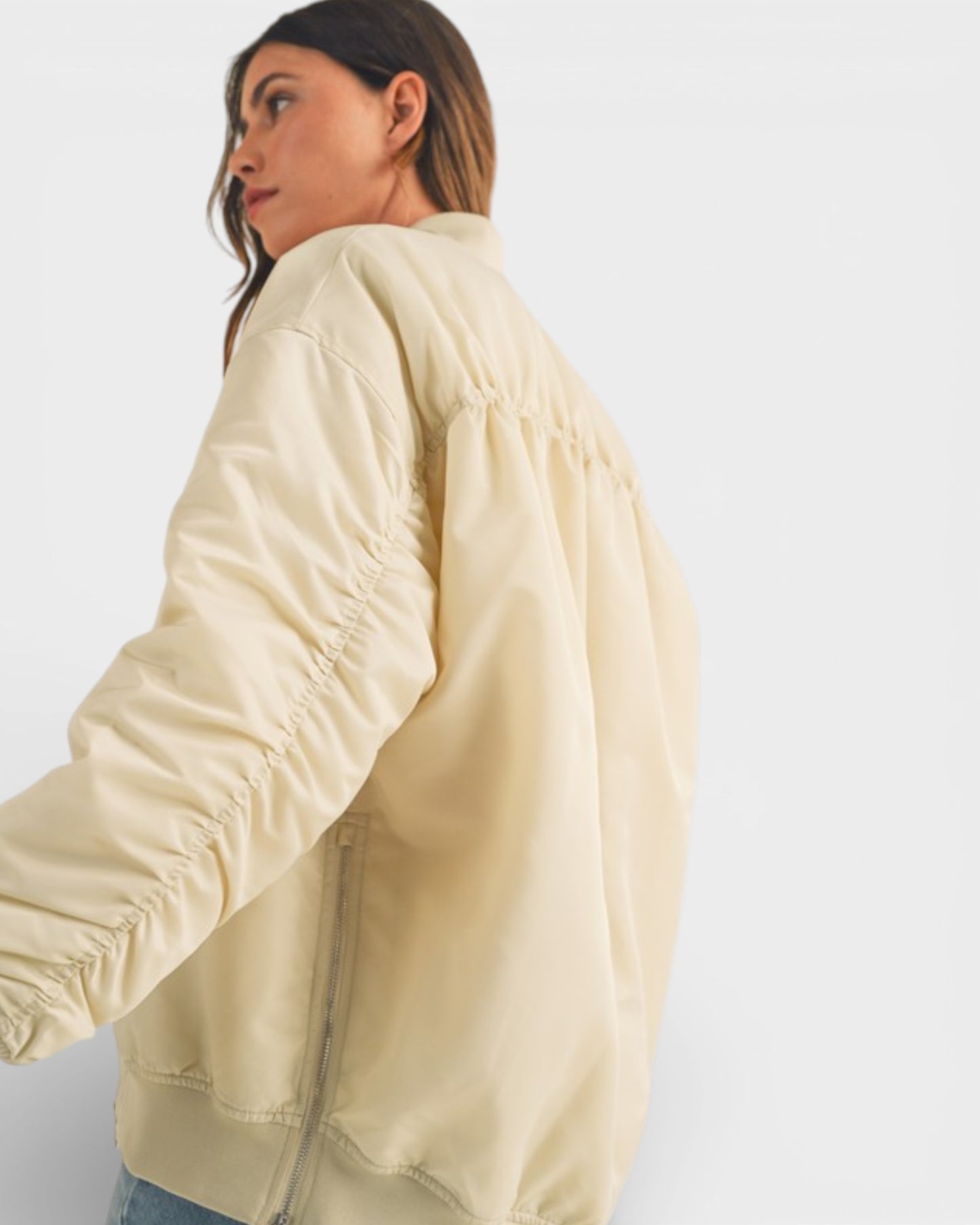 Woman wearing a light yellow bomber jacket on a plain background