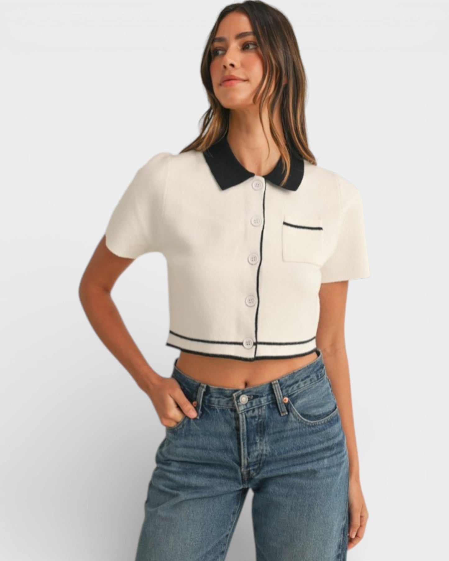 Woman wearing a white cropped shirt with black trim and blue jeans on a light gray background