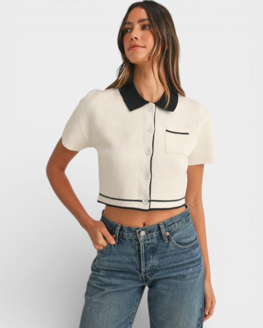 Woman wearing a white cropped shirt with black trim and blue jeans on a light gray background