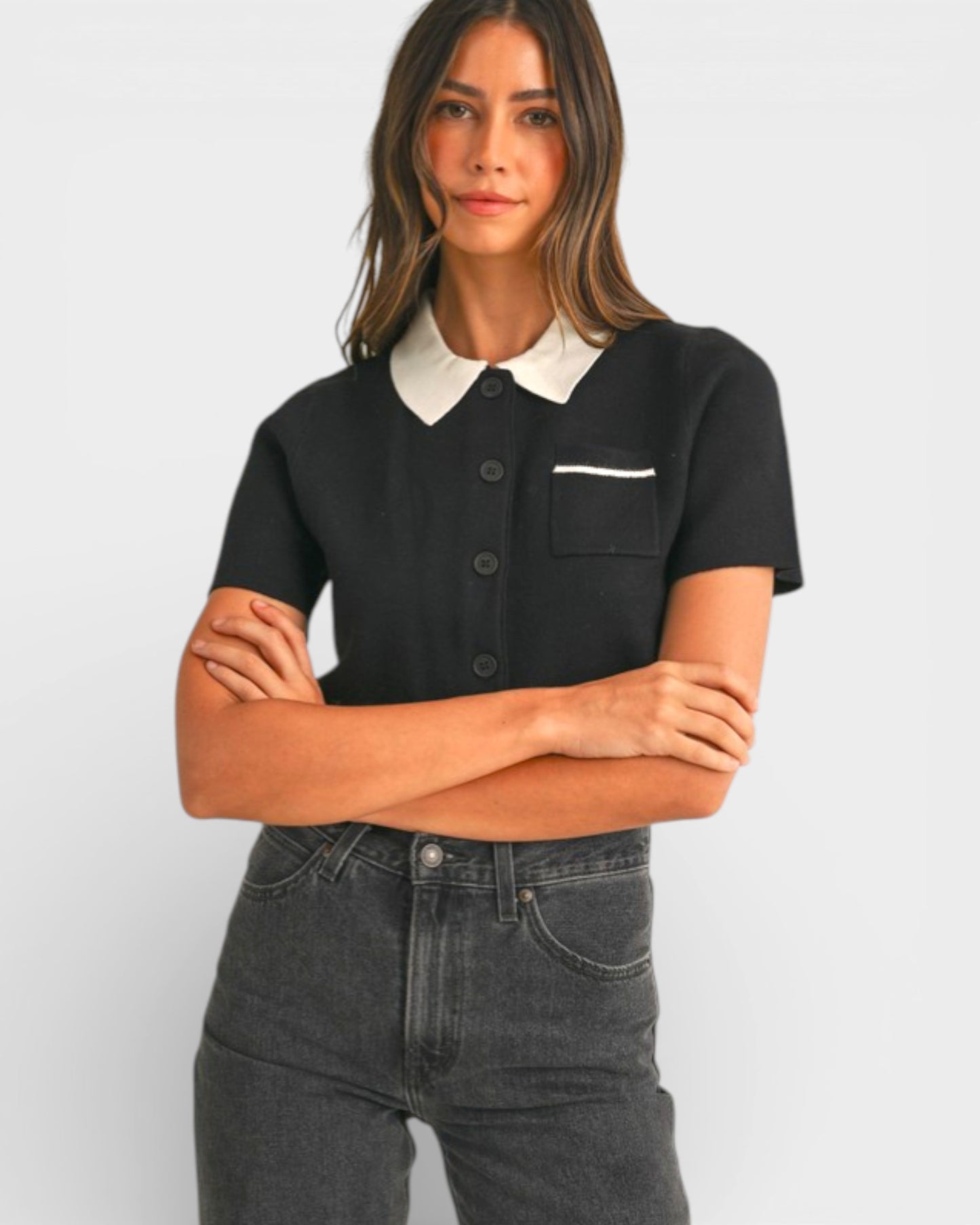 Woman wearing a black and white polo shirt with arms crossed on a plain background