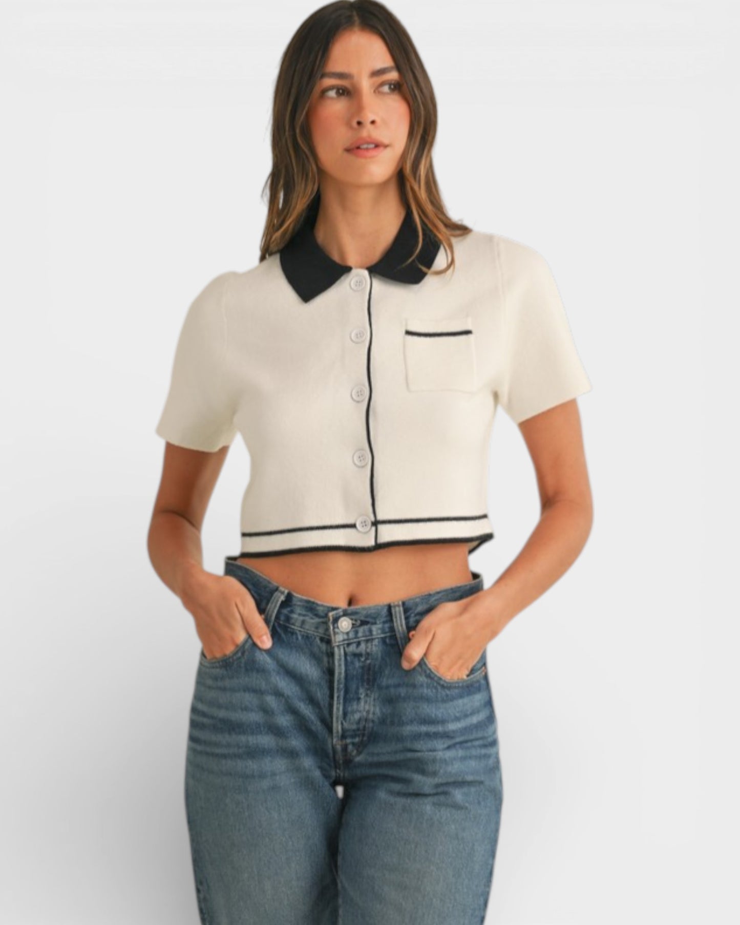 Woman wearing a white cropped shirt with black collar and trim, paired with blue jeans on a white background