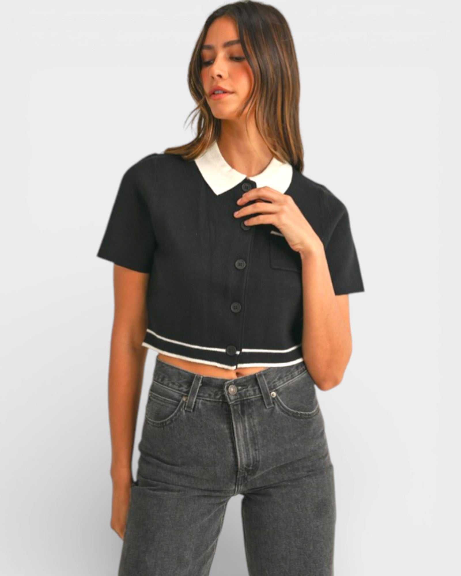 Woman wearing a black cropped shirt with a white collar and gray jeans on a light gray background