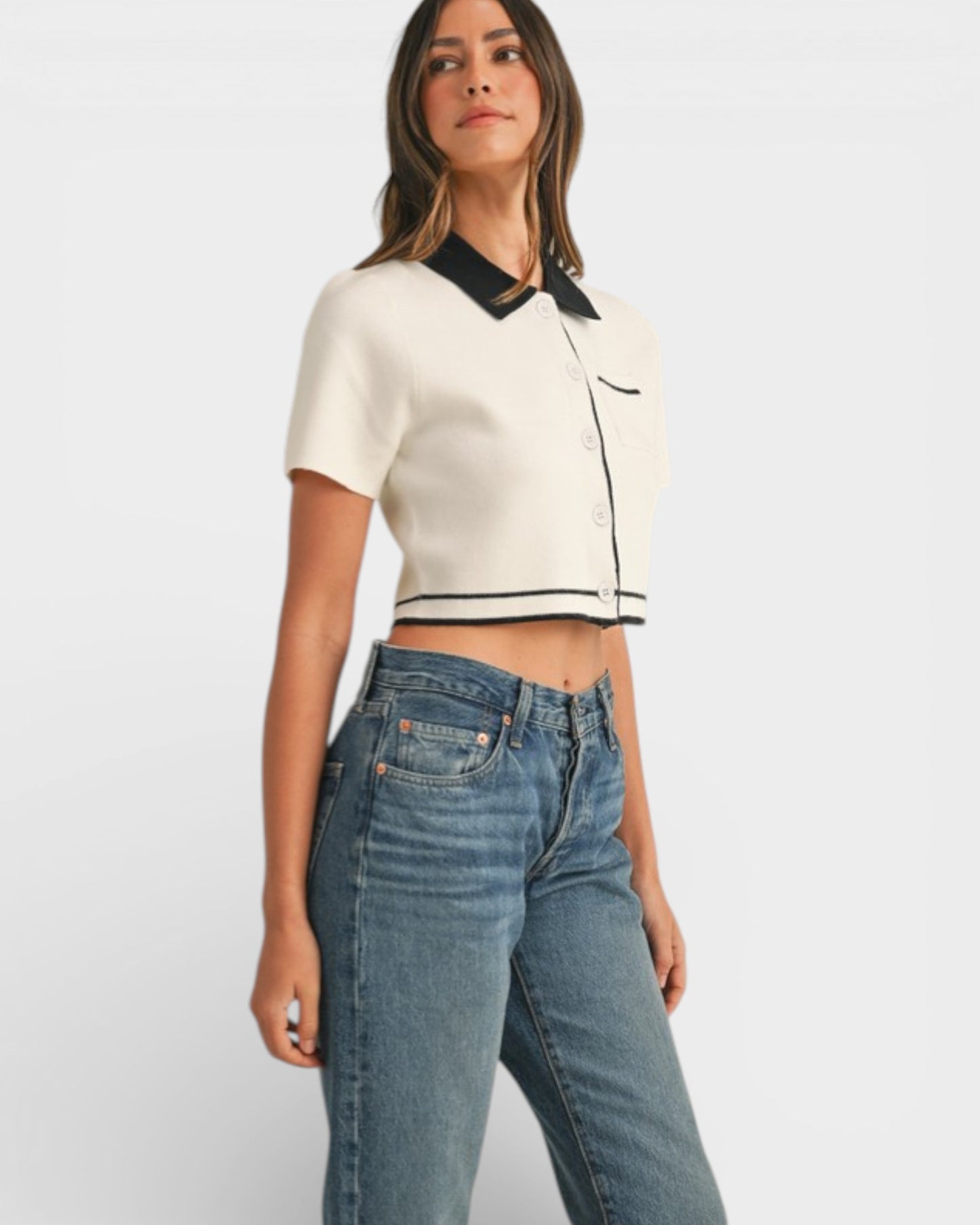 Woman wearing a white cropped top with black trim and blue jeans on a light gray background