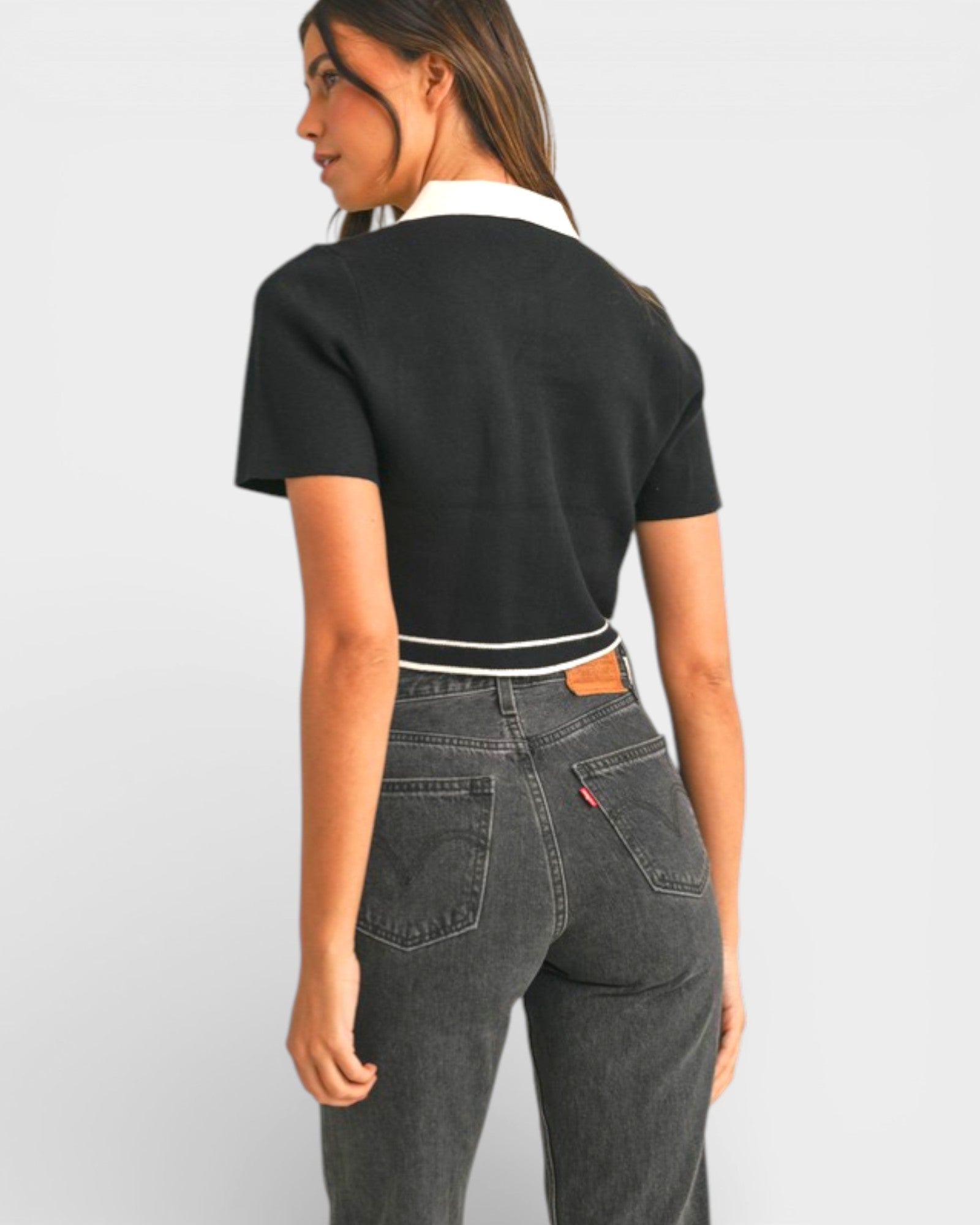 Person wearing a black crop top and gray jeans on a light gray background