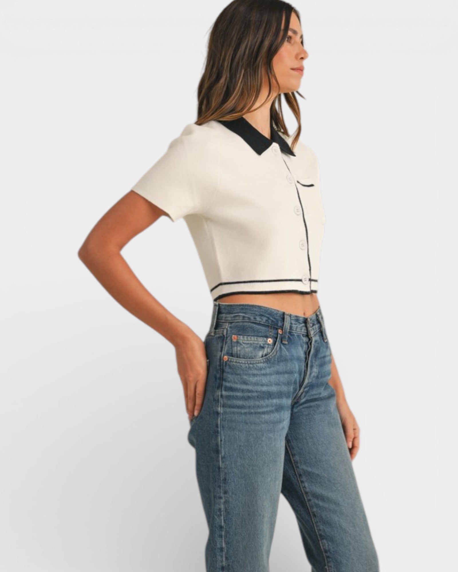 Woman wearing a white and black cropped top with blue jeans on a white background