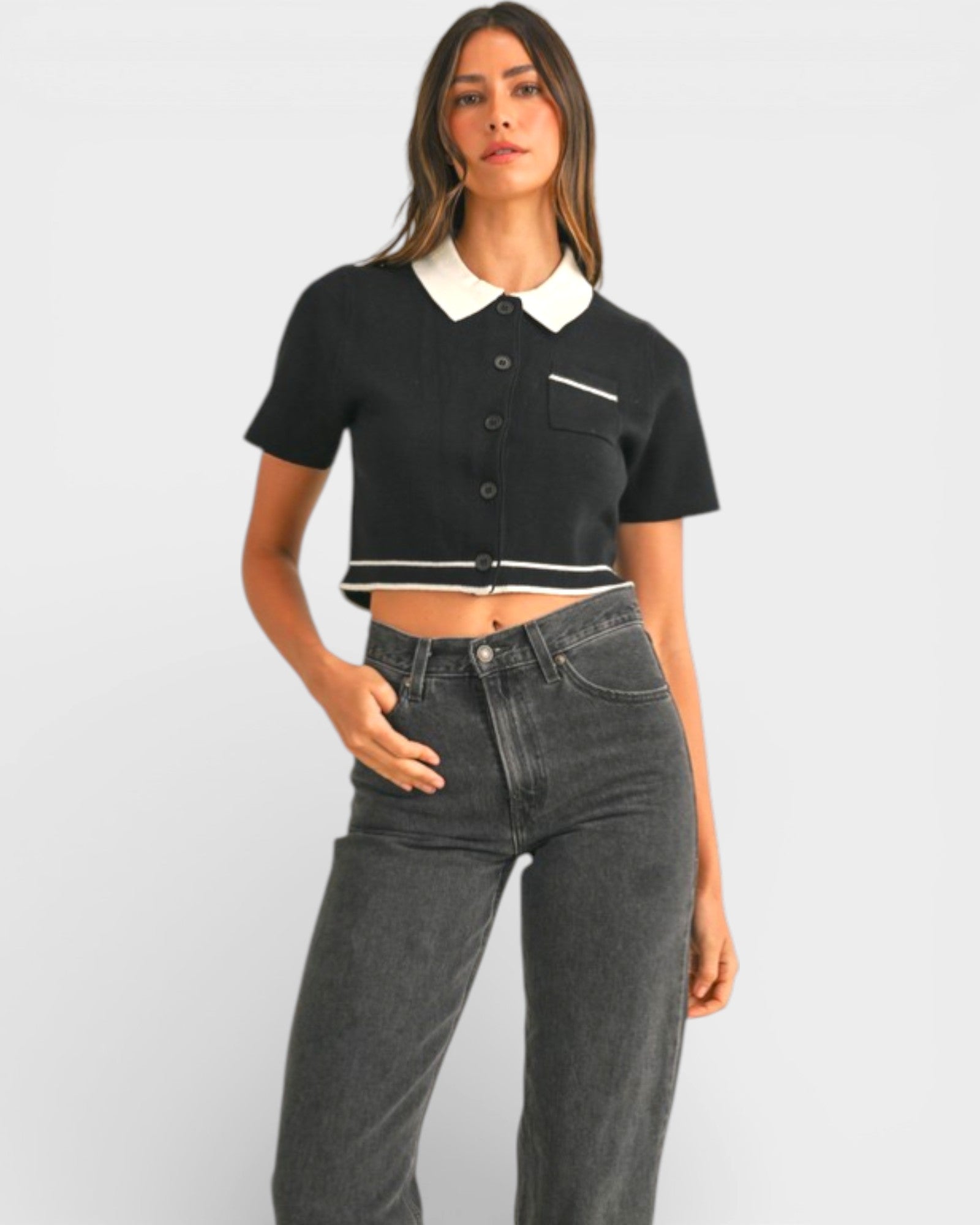 Woman wearing a black cropped top with white collar and gray jeans on a light gray background