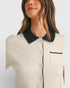 Woman wearing a white blouse with black collar and trim on a light gray background