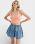 Woman wearing a peach tank top and denim shorts on a white background