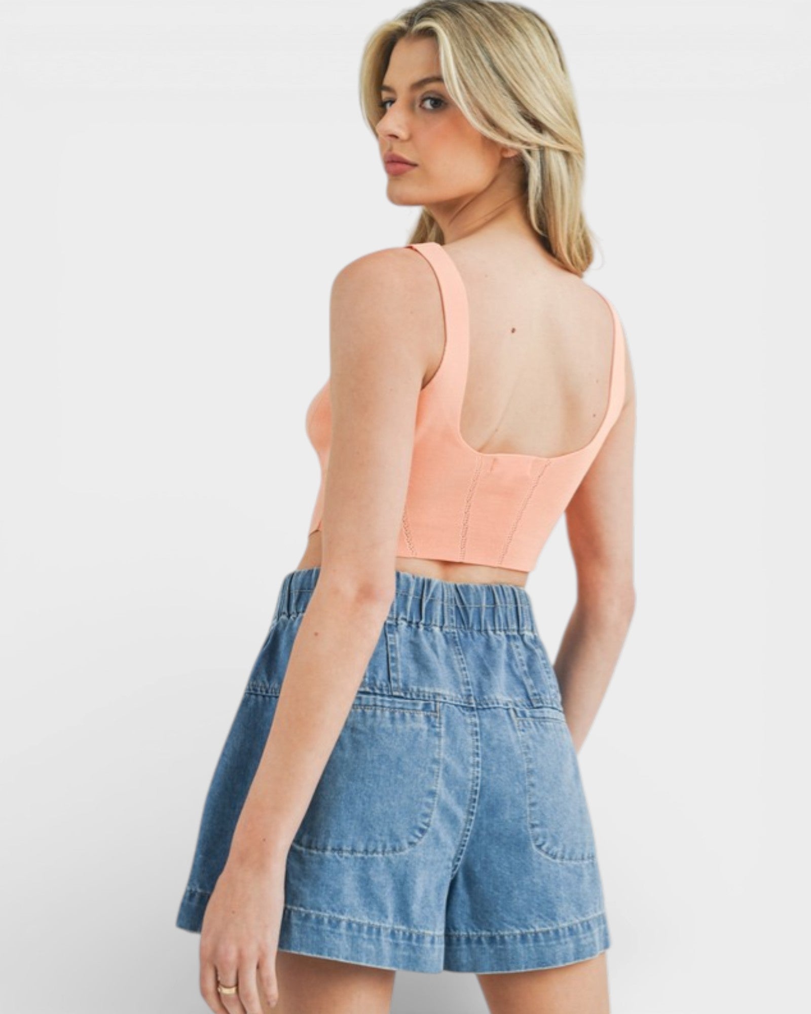 Woman wearing a peach crop top and denim shorts on a white background