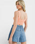 Woman wearing a peach crop top and denim shorts on a white background