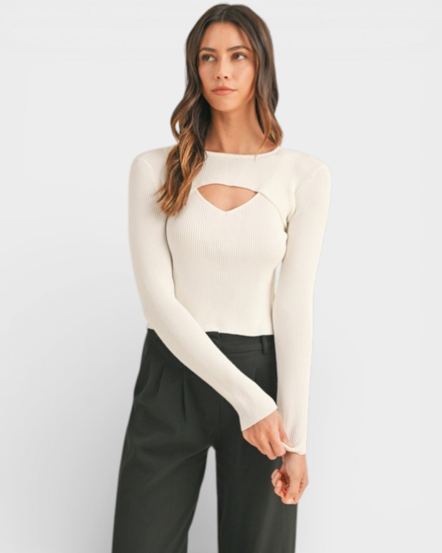 Woman wearing a cream long-sleeve top with cut-out design and black pants on a white background
