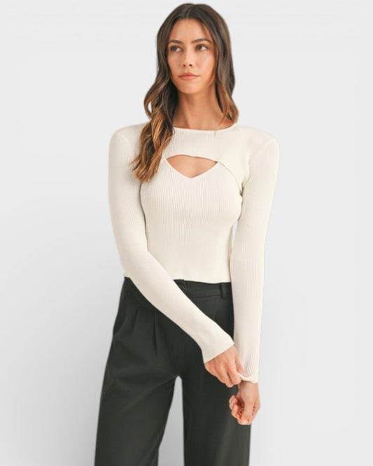 Woman wearing a cream long-sleeve top with cut-out design and black pants on a white background
