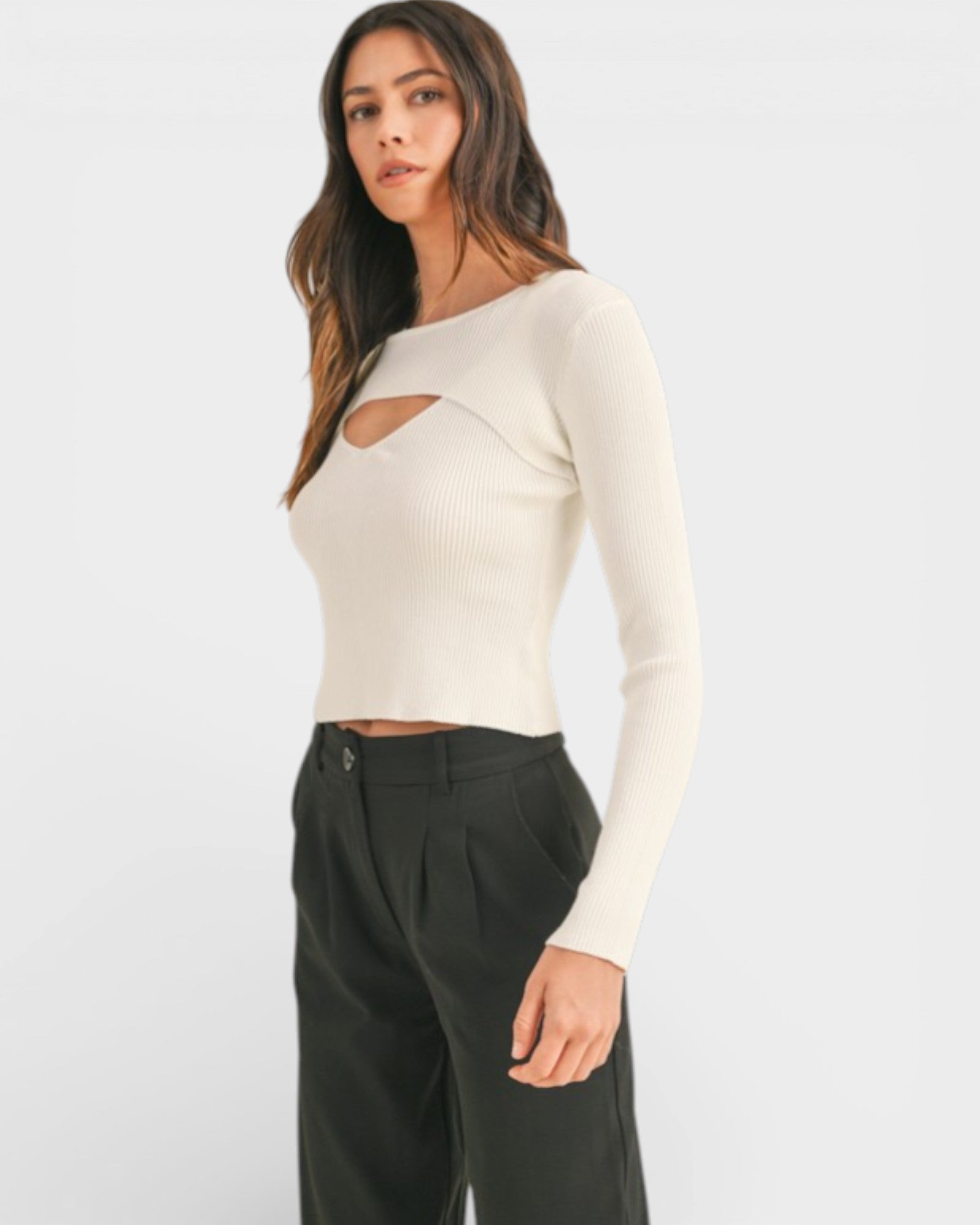 Woman wearing a white long-sleeve top with cut-out design and black pants on a white background