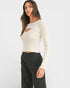 Woman wearing a white long-sleeve top with cut-out design and black pants on a white background