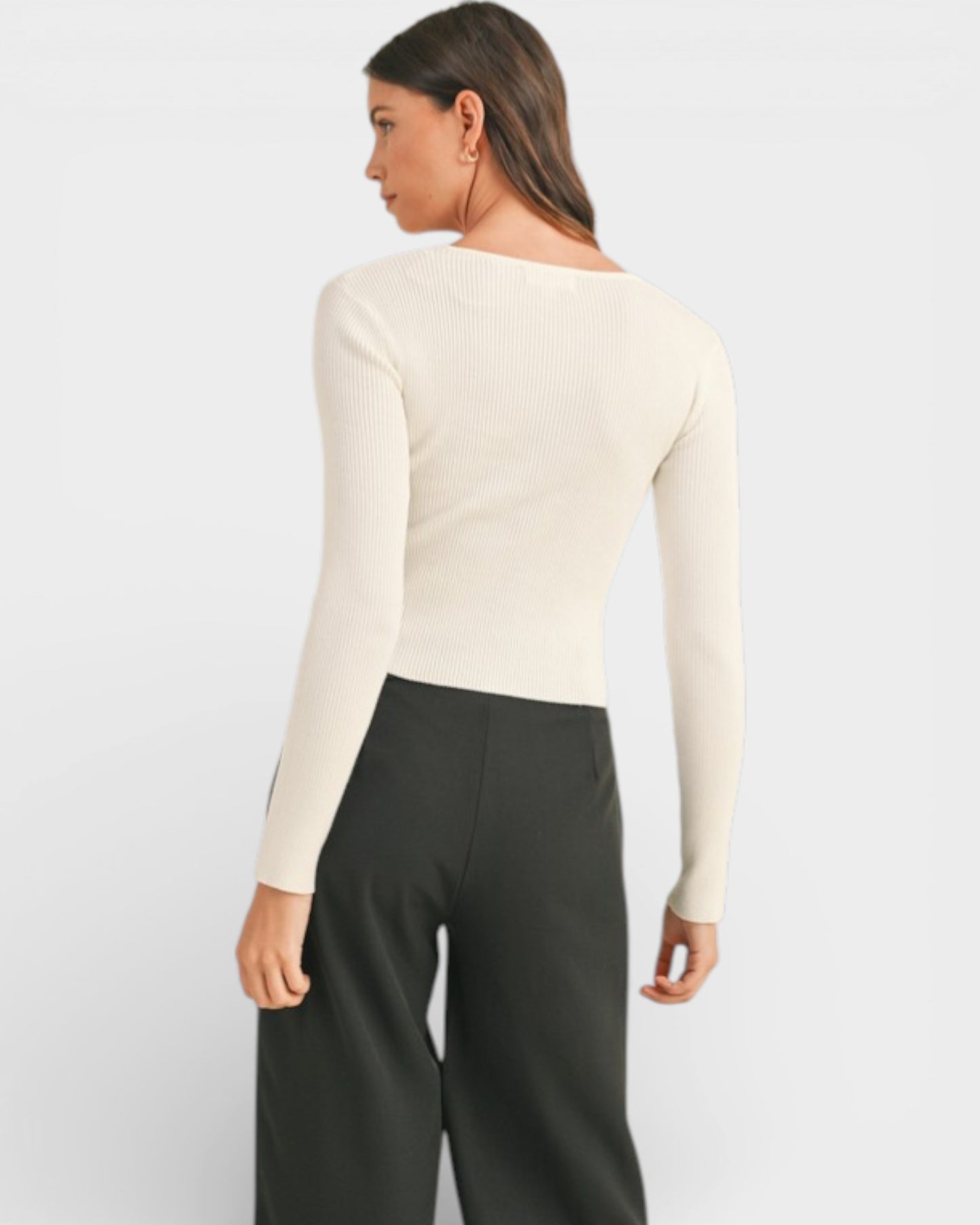 Person wearing a cream long-sleeve top and black pants on a light gray background