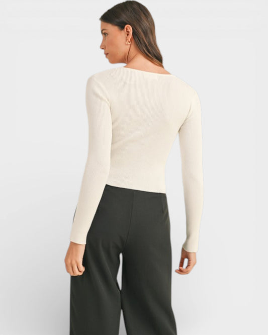 Person wearing a cream long-sleeve top and black pants on a light gray background