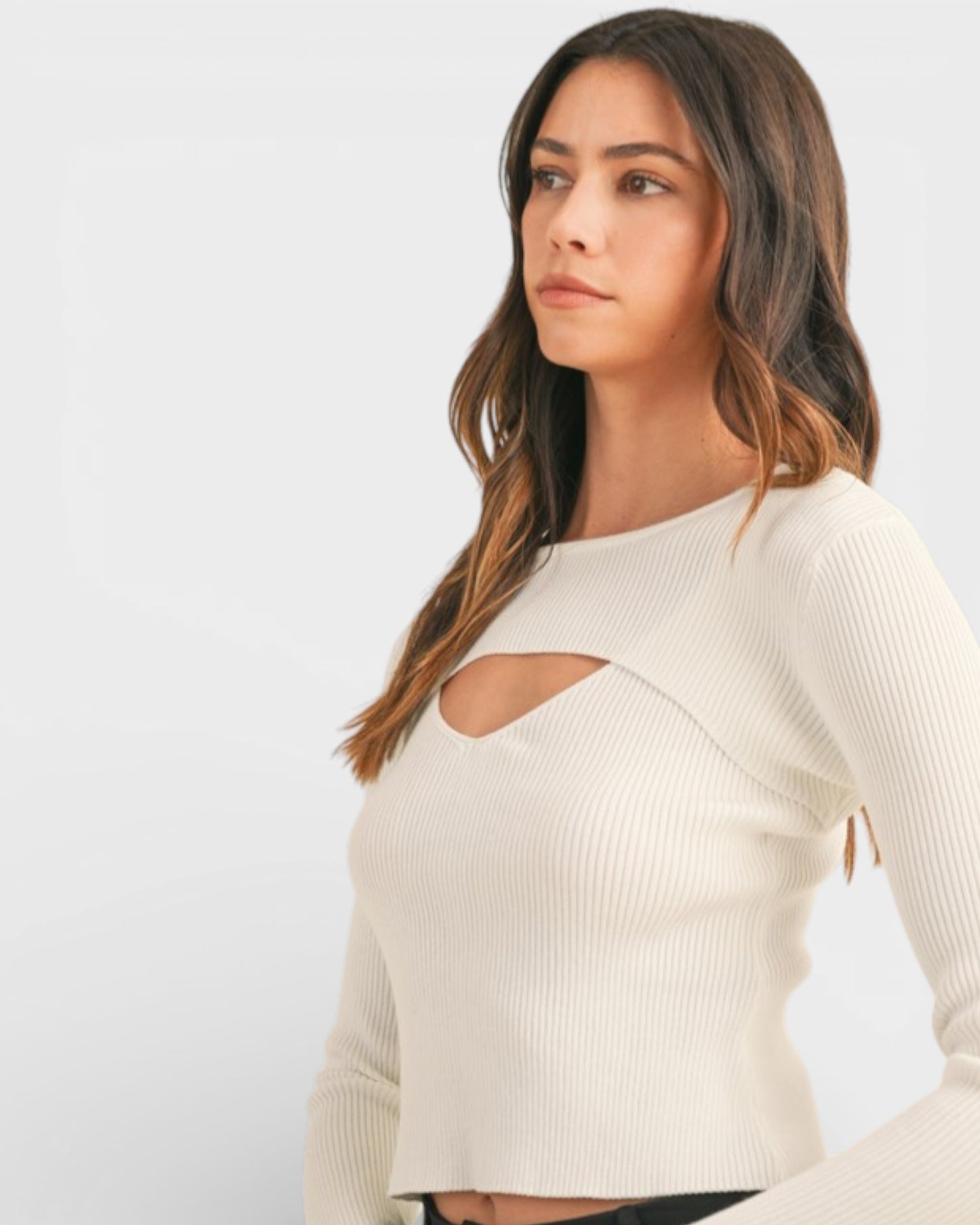 Woman wearing a beige long-sleeve top with cut-out design on a light gray background