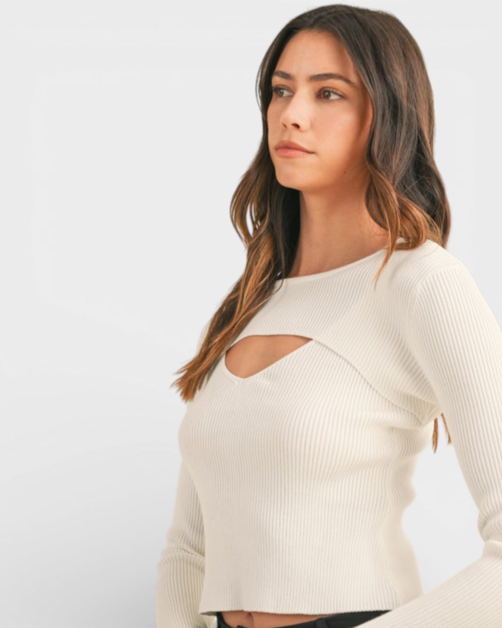 Woman wearing a beige long-sleeve top with cut-out design on a light gray background