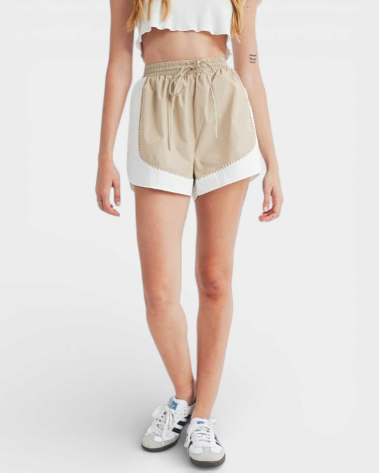 Person wearing beige shorts with white trim on a plain background