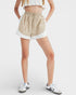 Person wearing beige shorts with white trim on a plain background