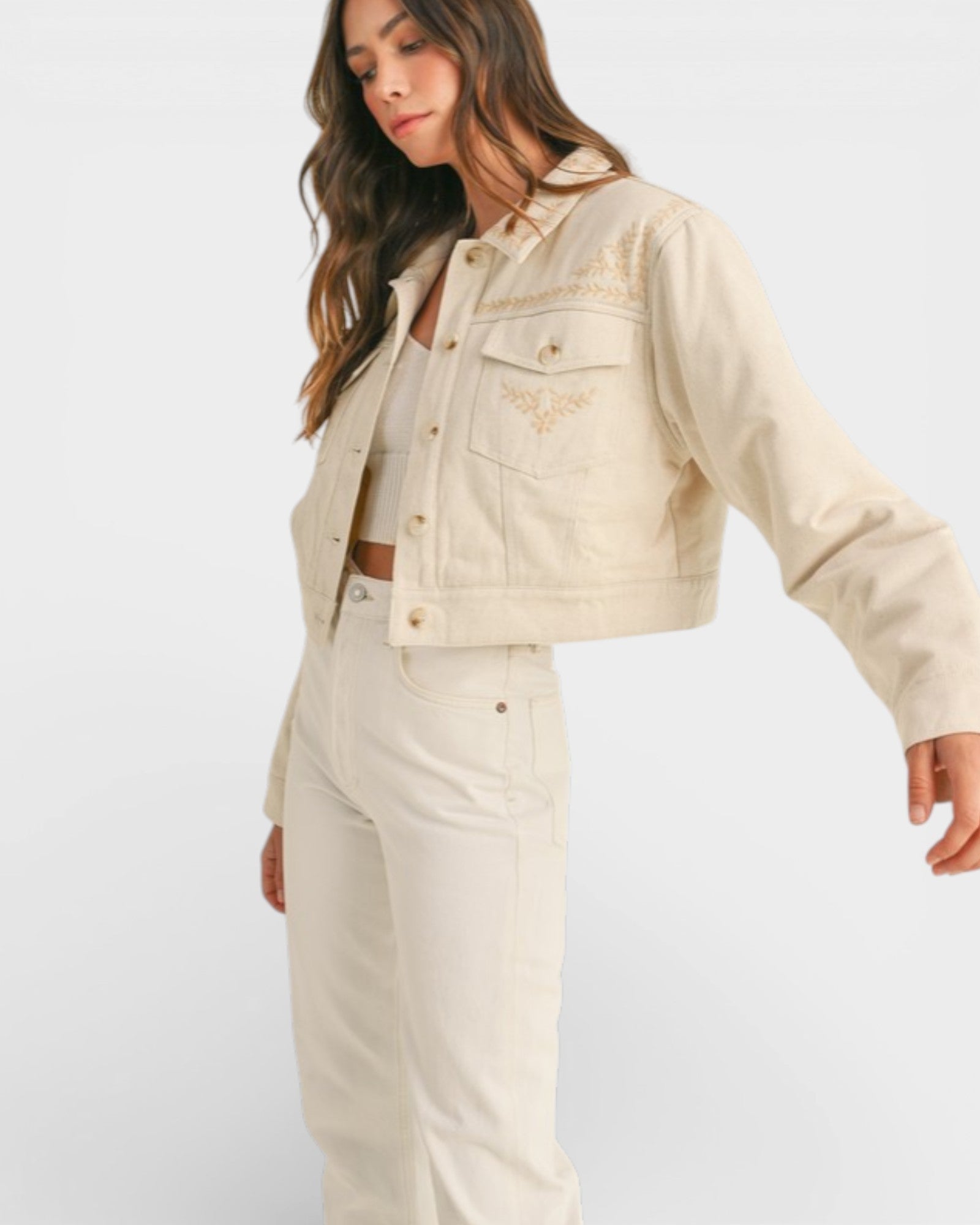 Woman wearing a beige denim jacket with floral embroidery on a white background