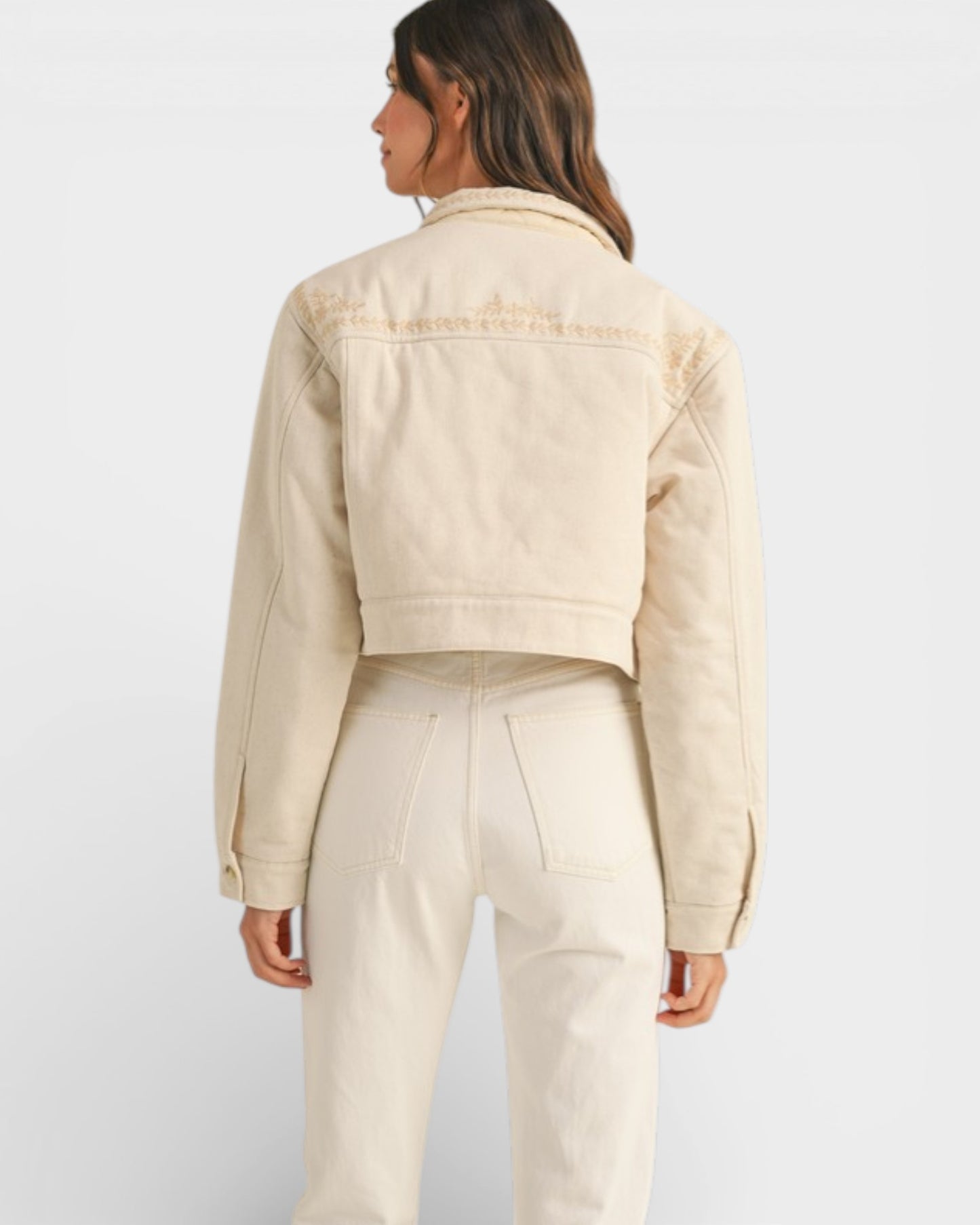 Person wearing a beige denim jacket and pants on a white background