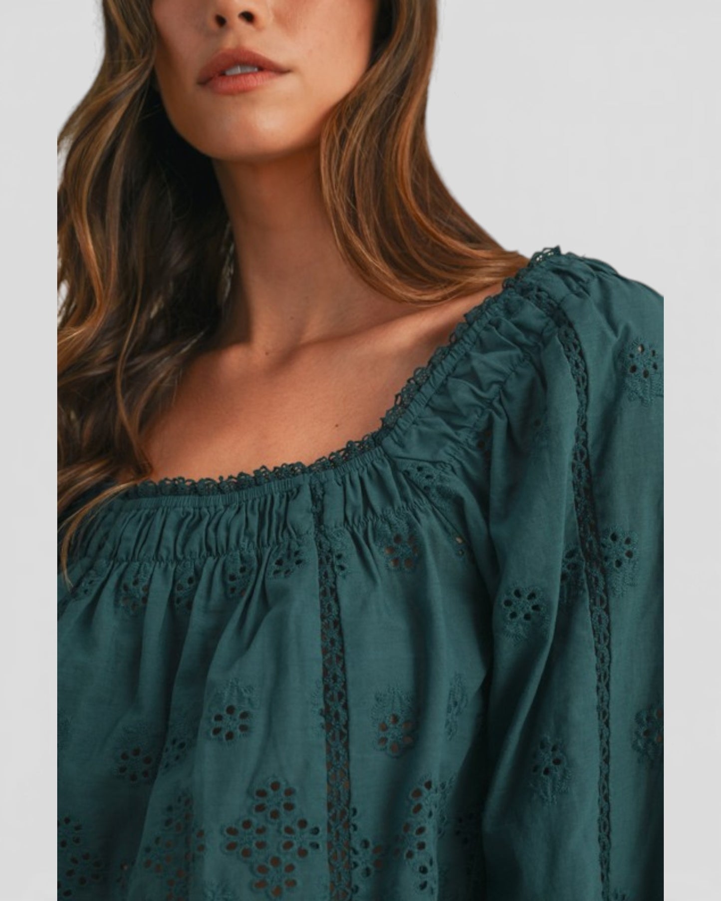 Woman wearing a green blouse with intricate detailing on a plain background