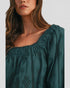 Woman wearing a green blouse with intricate detailing on a plain background
