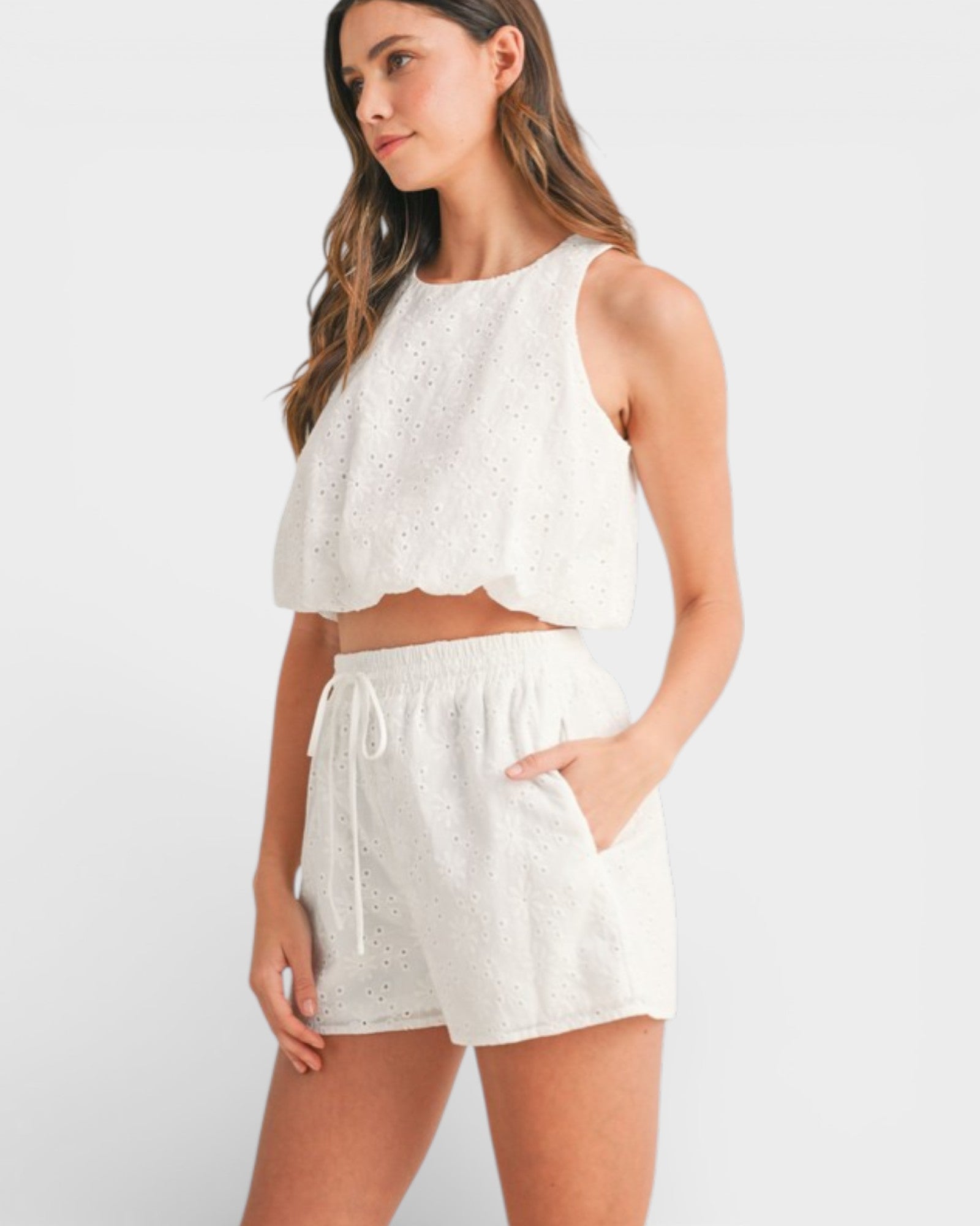 Woman wearing a white outfit with a top and shorts on a plain background