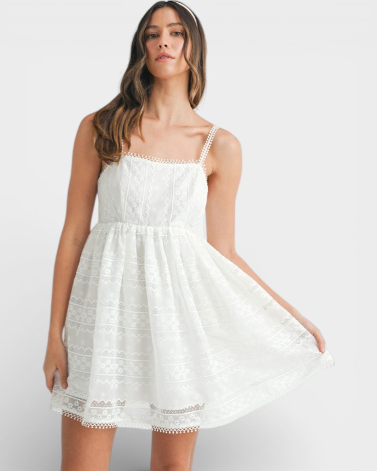 Woman wearing a white dress with lace details on a plain background