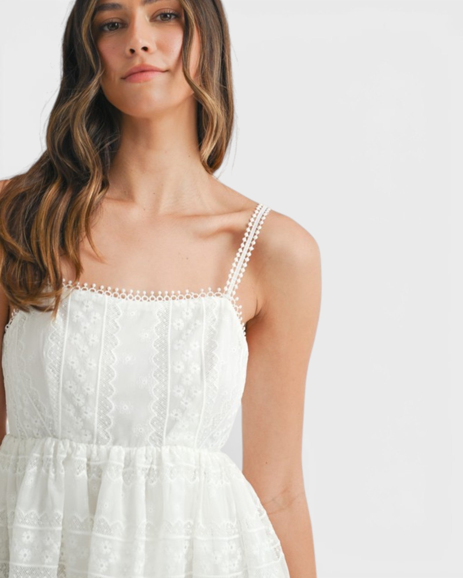Woman wearing a white dress with thin straps on a plain background