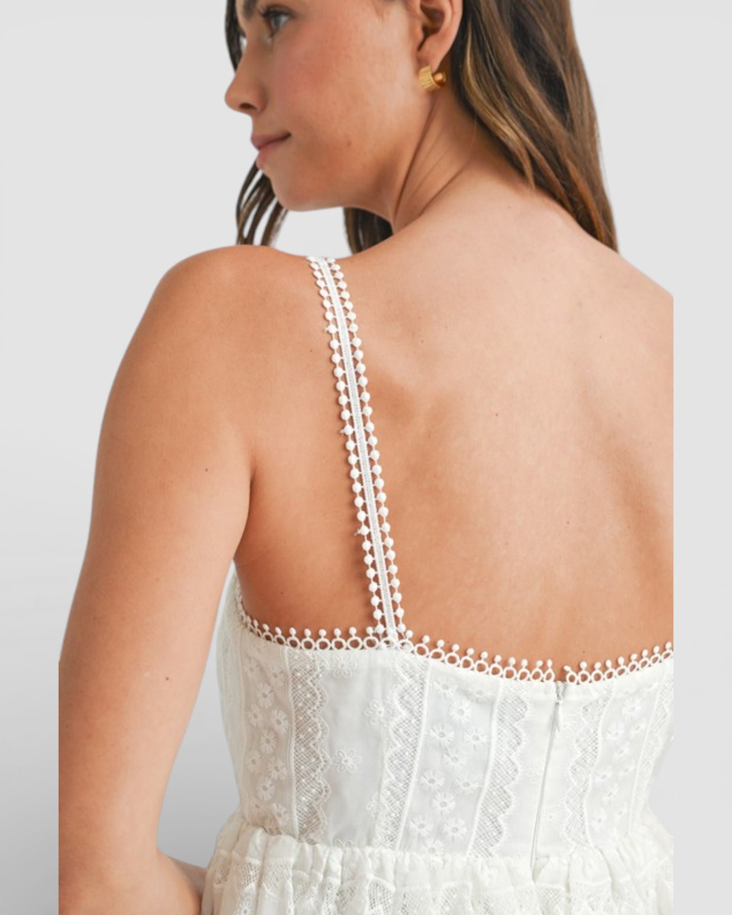 Woman wearing a white lace dress with thin straps against a light gray background