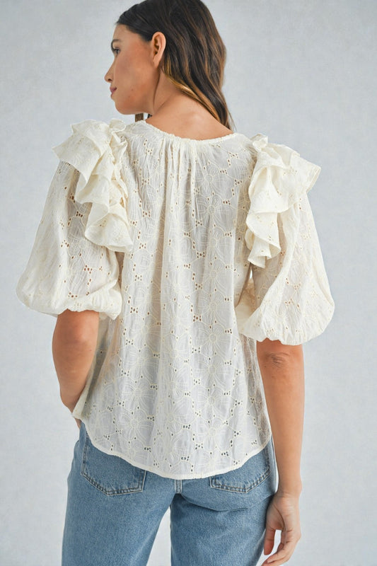 Woman wearing a white blouse with ruffled sleeves and blue jeans on a plain background