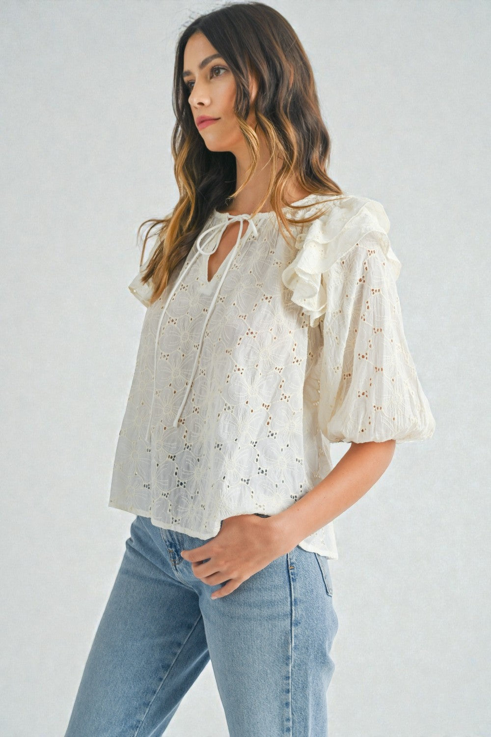 Woman wearing a white lace blouse with ruffled sleeves and blue jeans on a white background