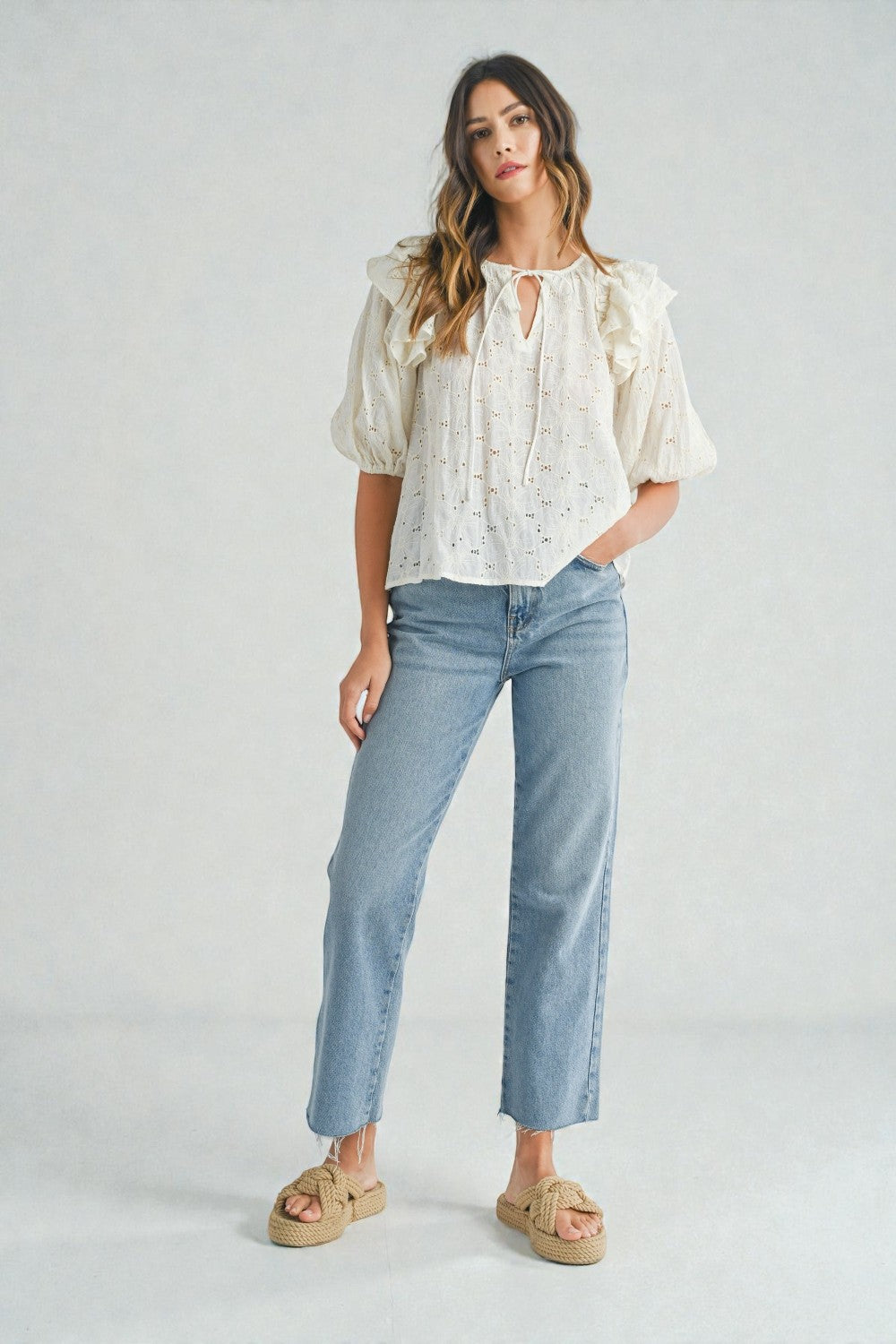 Woman wearing a white blouse and light blue jeans on a plain background
